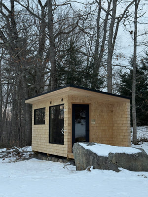 Searsmont, Maine custom sauna — full exterior in winter, cedar shingles under a black standing seam roof