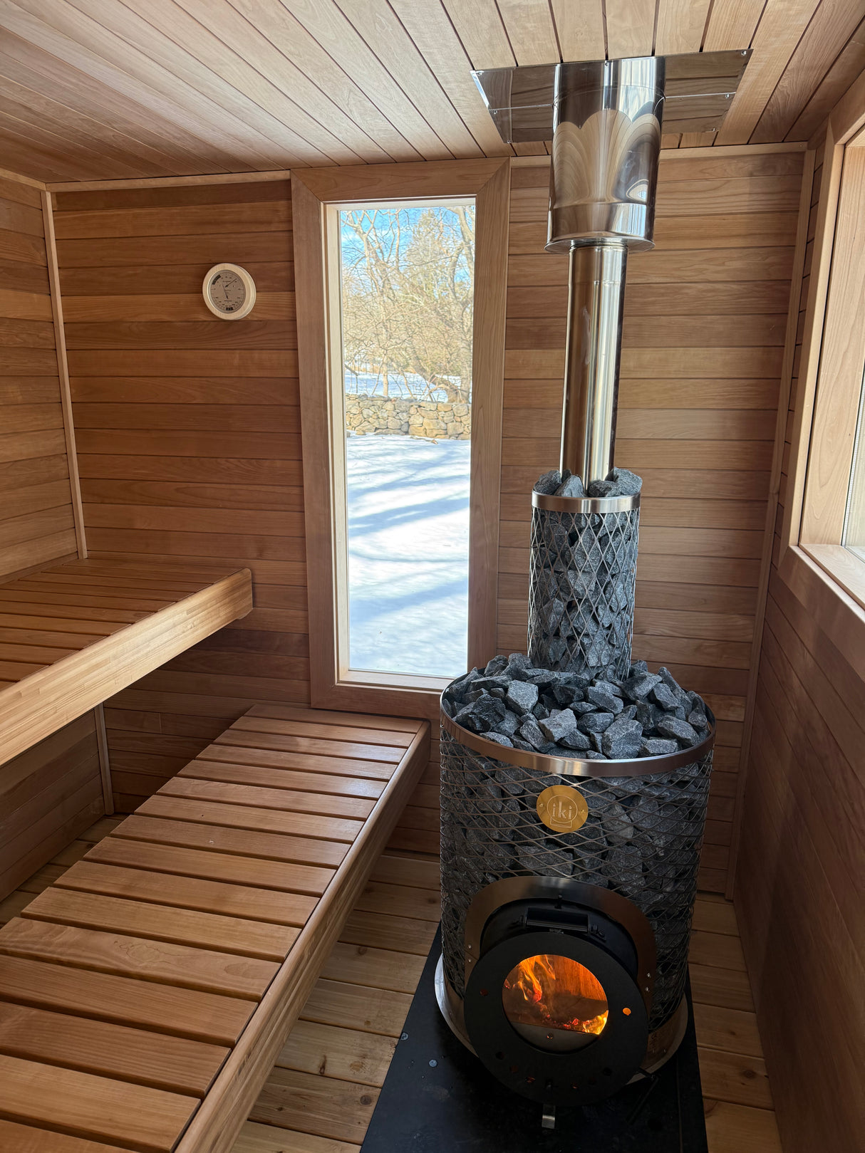 Wilton, Connecticut custom sauna — exterior in snow, vertical cedar cladding and stainless chimney against snow-covered woods